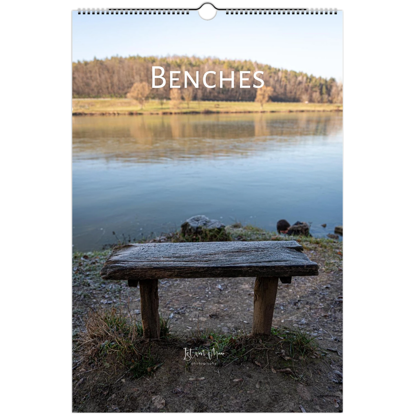 A wall calendar page featuring a scenic photograph of a rustic wooden bench by a calm lake, with the word 'BENCHES' printed across the top and a hanging hole at the top center.