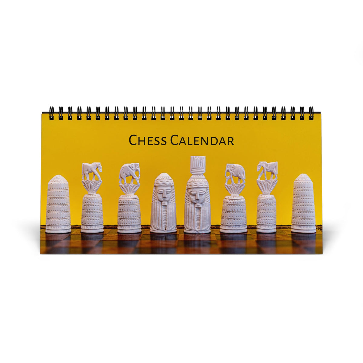 A spiral-bound desk calendar titled 'CHESS CALENDAR' with a bright yellow cover showing a row of white carved chess pieces on a dark wooden surface, photographed on a white background.