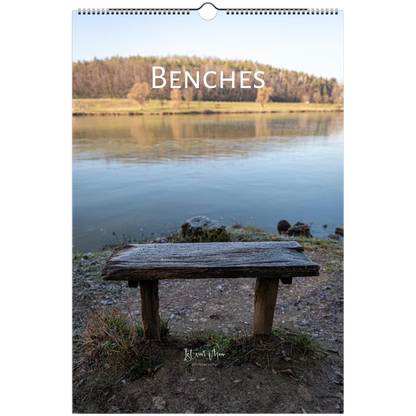 A wall calendar page featuring a scenic photograph of a rustic wooden bench by a calm lake, with the word 'BENCHES' printed across the top and a hanging hole at the top center.
