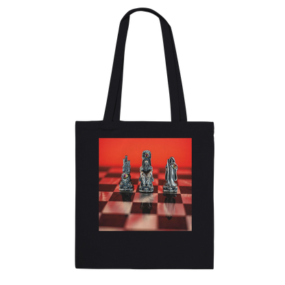 A black canvas tote bag with two shoulder straps, featuring a rectangular printed graphic on the front of three metallic chess pieces on a red and black checkered board against a red background.
