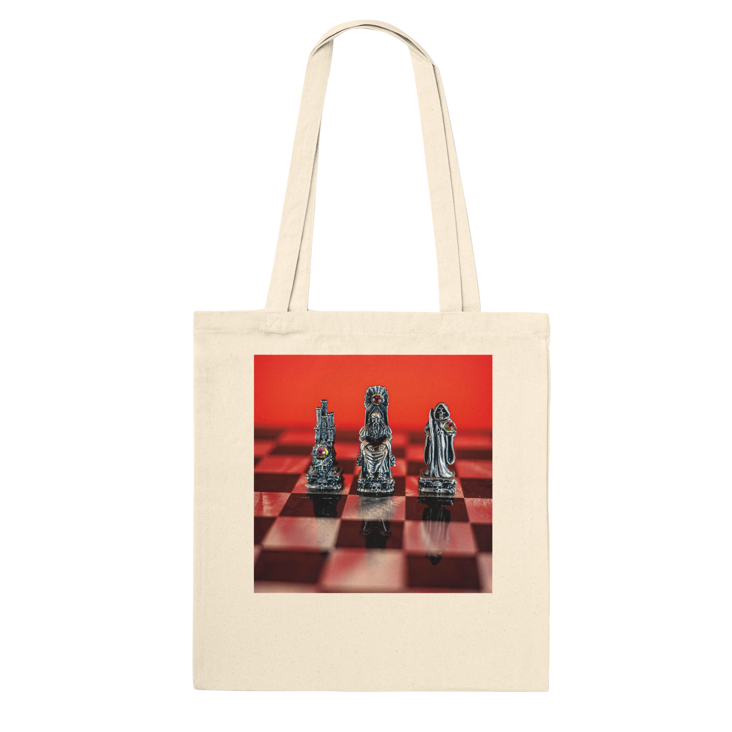 A cream canvas tote bag with a square graphic print on the front showing three metallic chess pieces on a red and black checkered board against a bright red background.