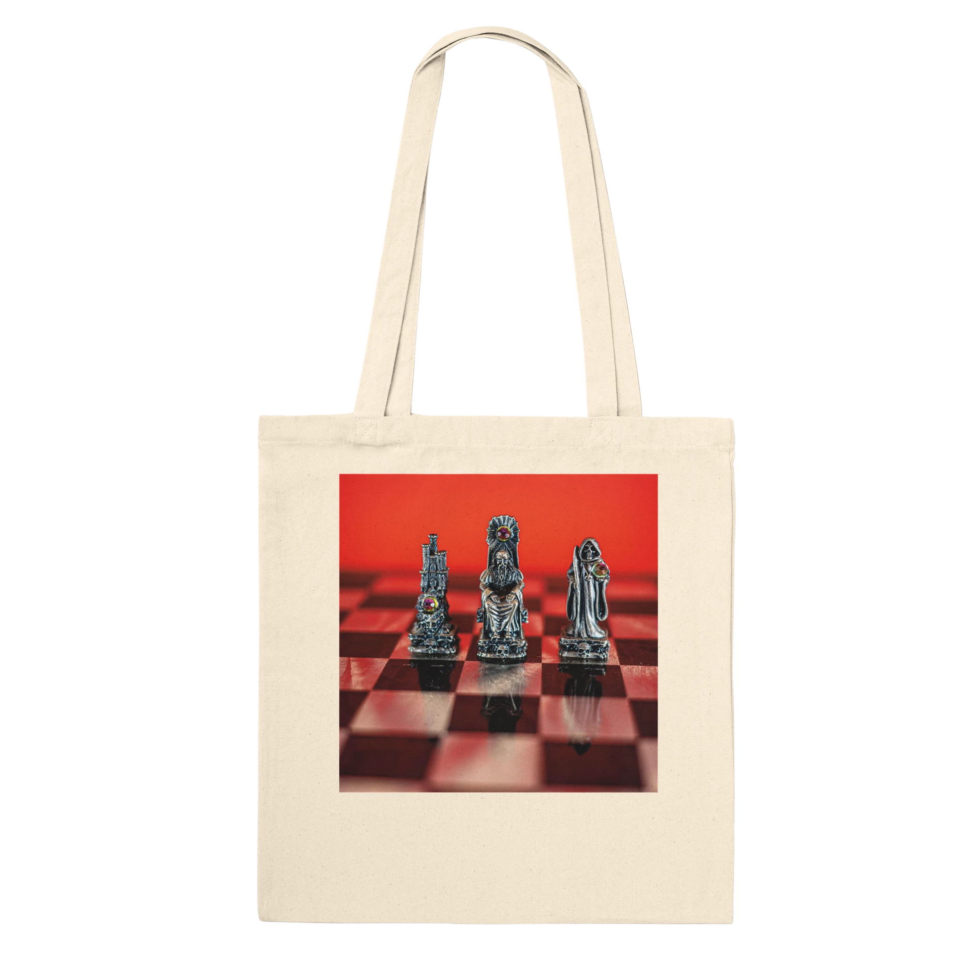 A cream canvas tote bag with a square graphic print on the front showing three metallic chess pieces on a red and black checkered board against a bright red background.