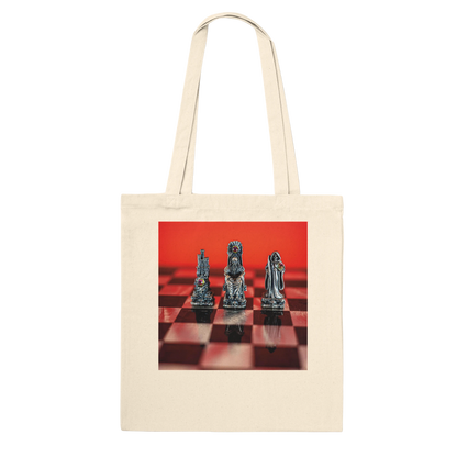 A cream canvas tote bag with a square graphic print on the front showing three metallic chess pieces on a red and black checkered board against a bright red background.