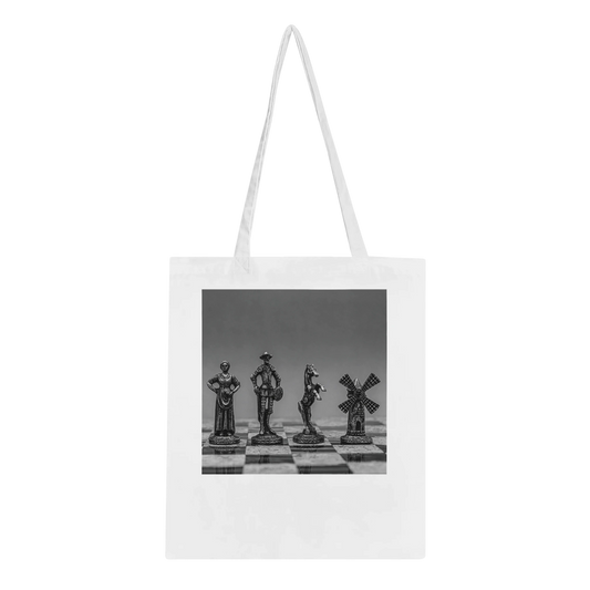A white canvas tote bag with long shoulder straps, featuring a black and white photographic print of four chess pieces on a chessboard. The bag is shown against a plain white background.