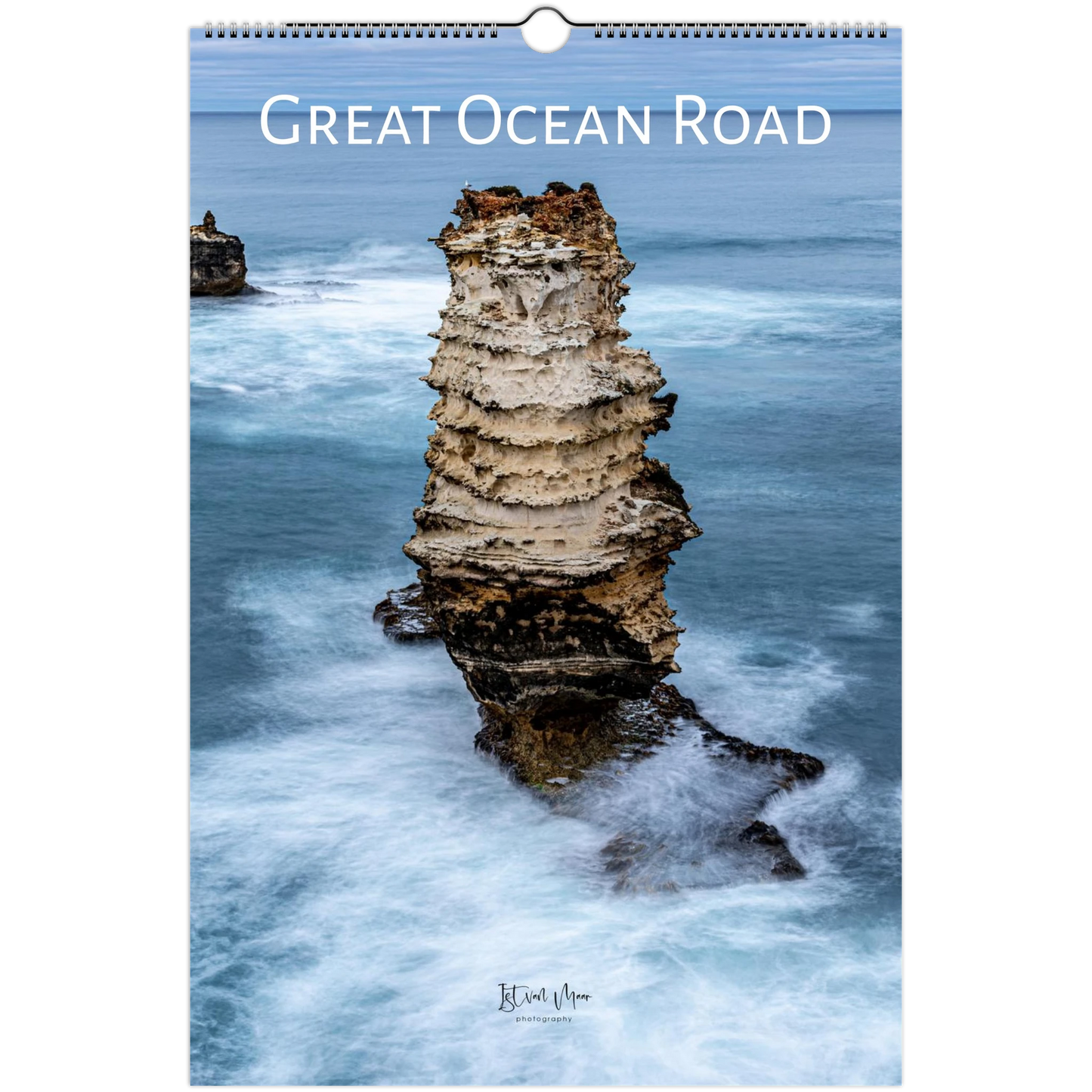 A spiral-bound wall calendar featuring a coastal photograph of a tall sea stack in the Great Ocean Road, with the title printed across the top and a small artist signature near the bottom.