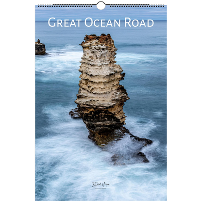 A spiral-bound wall calendar featuring a coastal photograph of a tall sea stack in the Great Ocean Road, with the title printed across the top and a small artist signature near the bottom.