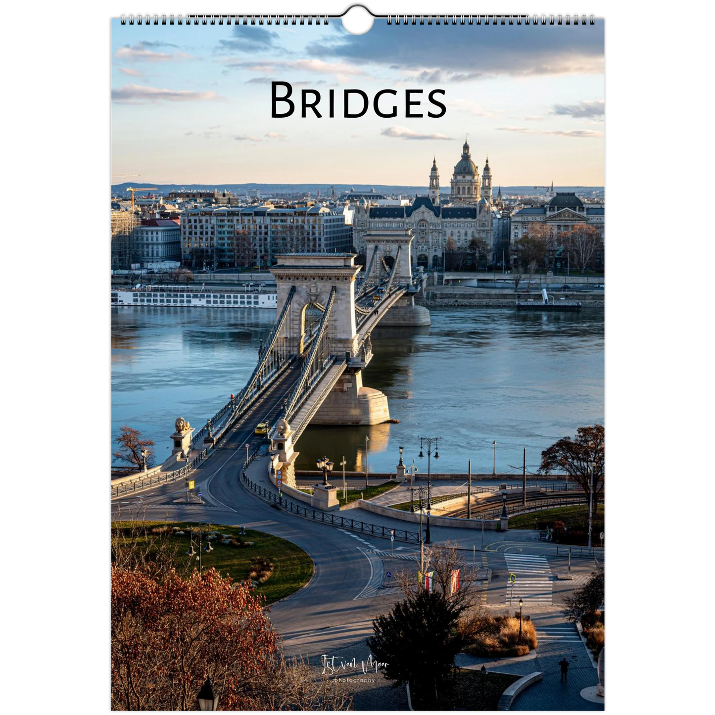 A vertical wall calendar page titled "BRIDGES" showing a scenic photograph of a suspension bridge over a river with city buildings in the background, photographed against a white surround.