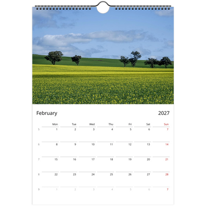 A single-page spiral-bound calendar page showing a landscape photograph of a yellow flower field under a blue sky, with a February 2027 calendar grid below. Ships worldwide.