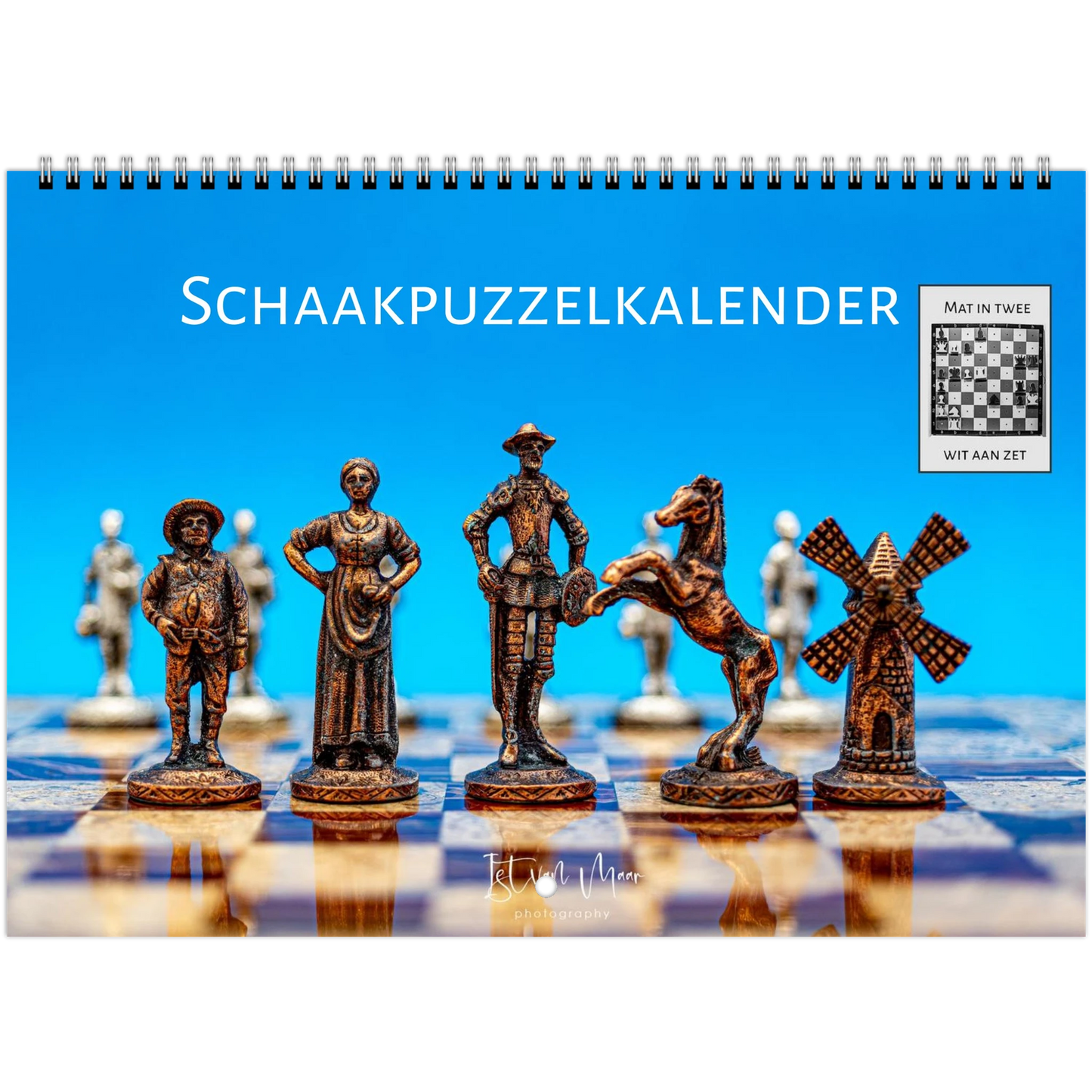 A spiral-bound desk calendar titled 'SCHAAKPUZZELKALENDER' featuring decorative chess pieces on a chessboard against a bright blue background, with a small inset showing a completed chessboard and the text 'MAT IN TWEE' and 'WIT AAN ZET'.