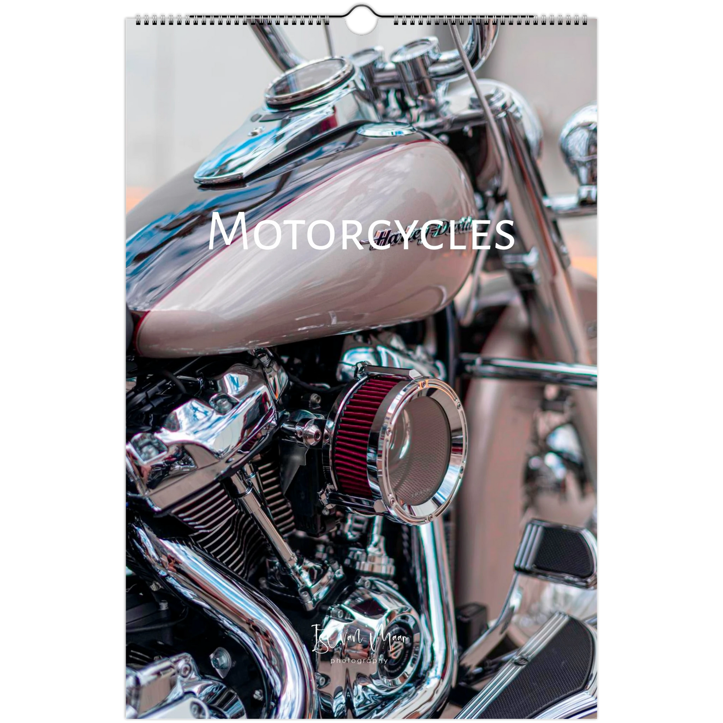A spiral-bound wall calendar page featuring a close-up photograph of a motorcycle, with the word 'MOTORCYCLES' printed across the center. The motorcycle has a metallic taupe gas tank, chrome engine components, and a red air filter.
