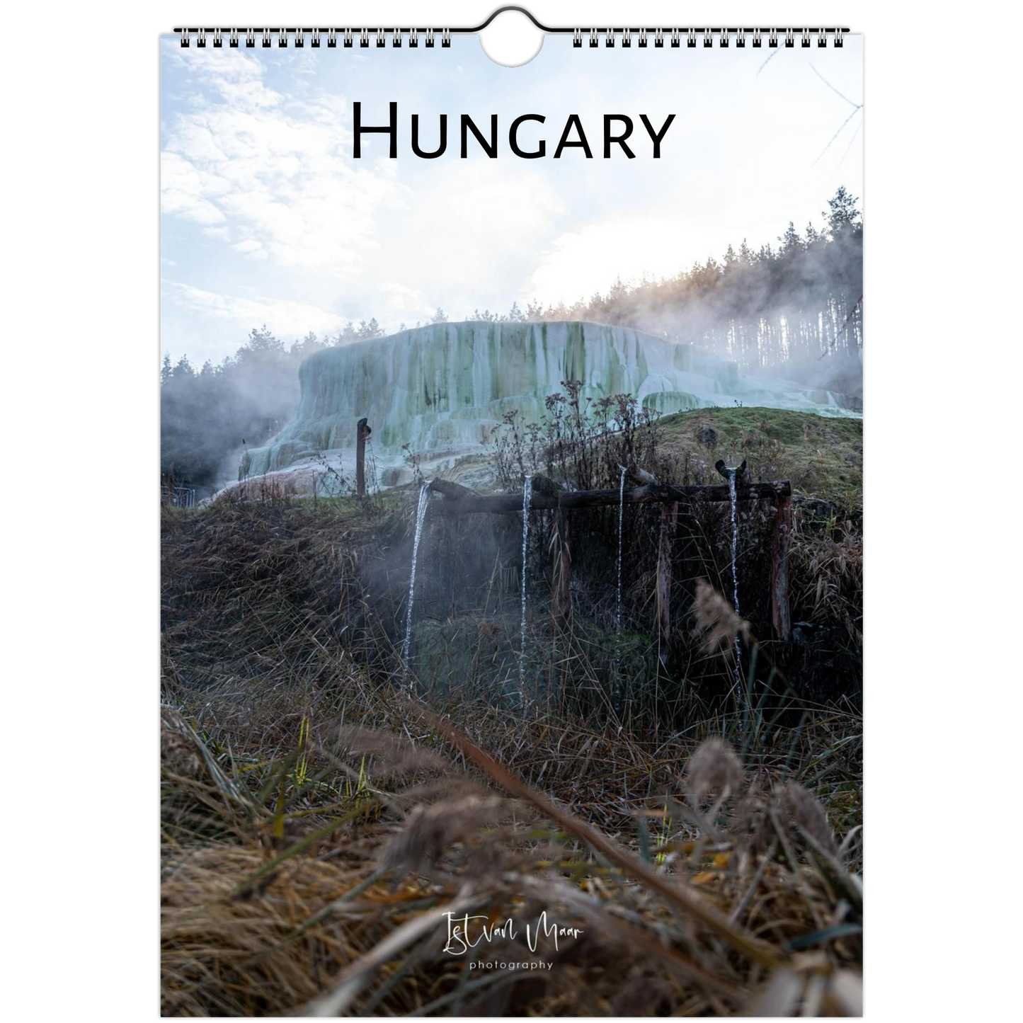 A hanging wall calendar or poster featuring a scenic photograph of a geothermal landscape in Hungary, with the word "HUNGARY" printed at the top and a spiral binding at the top edge. The scene shows steam, trees, and waterfalls in muted blue-green, brown, and gray tones.