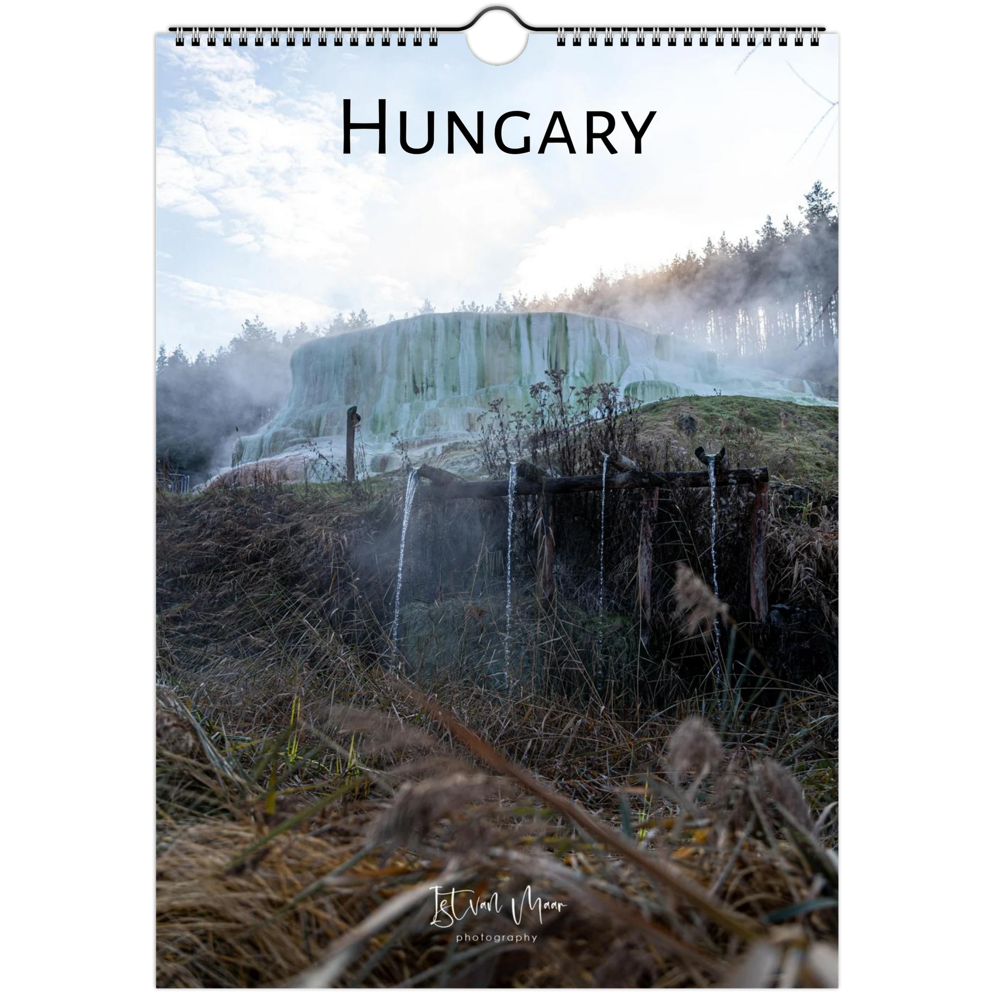 A hanging wall calendar or poster featuring a scenic photograph of a geothermal landscape in Hungary, with the word "HUNGARY" printed at the top and a spiral binding at the top edge. The scene shows steam, trees, and waterfalls in muted blue-green, brown, and gray tones.