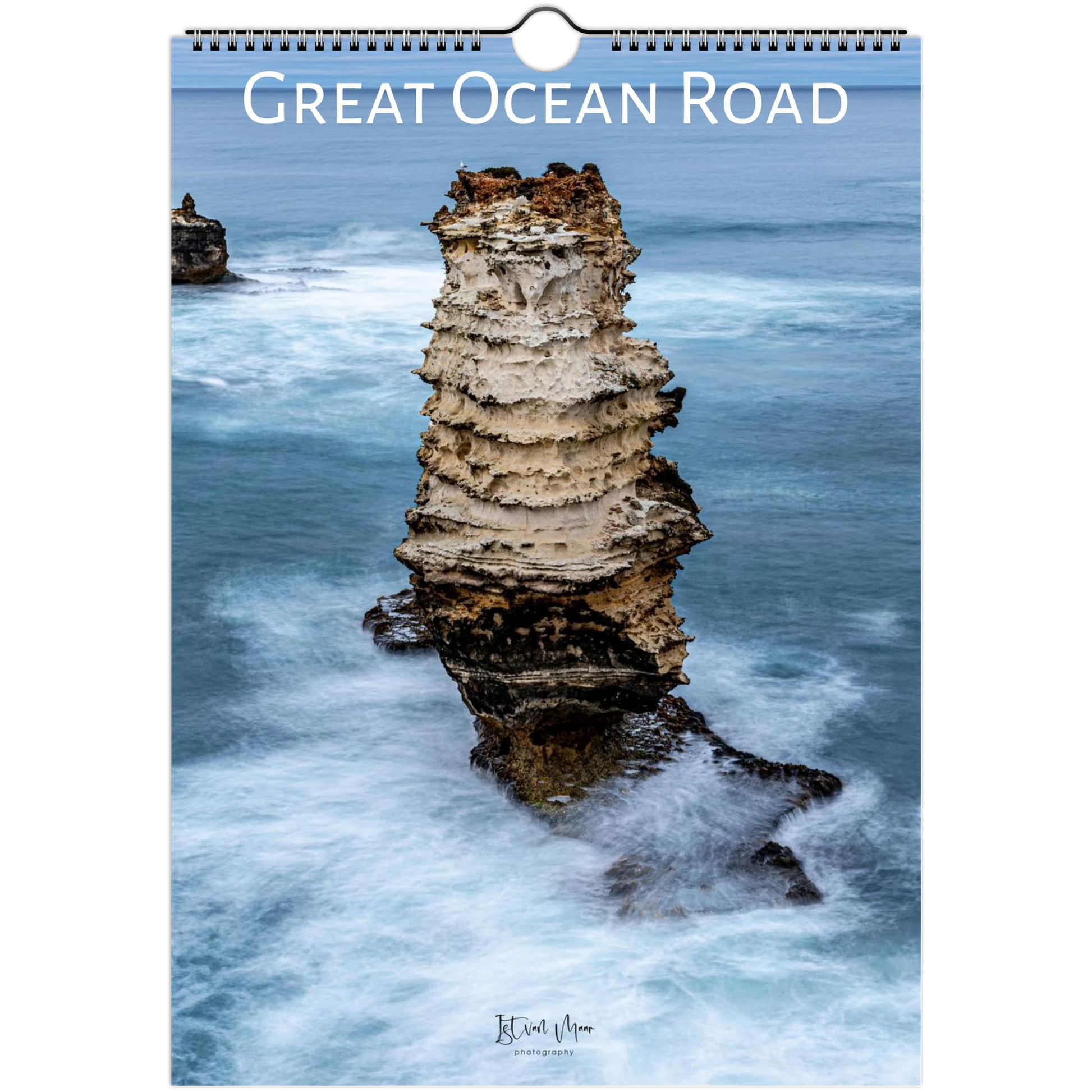 A spiral-bound wall calendar or print titled "Great Ocean Road" showing a coastal rock formation rising from blue ocean water, with the text "Great Ocean Road" across the top and a small artist signature near the bottom.