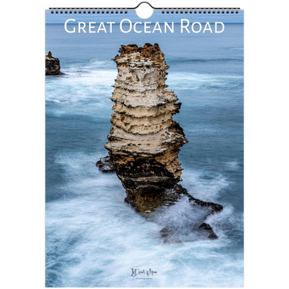 A spiral-bound wall calendar or print titled "Great Ocean Road" showing a coastal rock formation rising from blue ocean water, with the text "Great Ocean Road" across the top and a small artist signature near the bottom.
