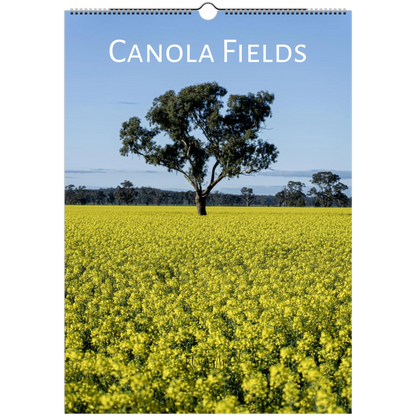 A spiral-bound wall calendar page showing a canola field with a single tree under a blue sky, with the title 'CANOLA FIELDS' printed at the top.