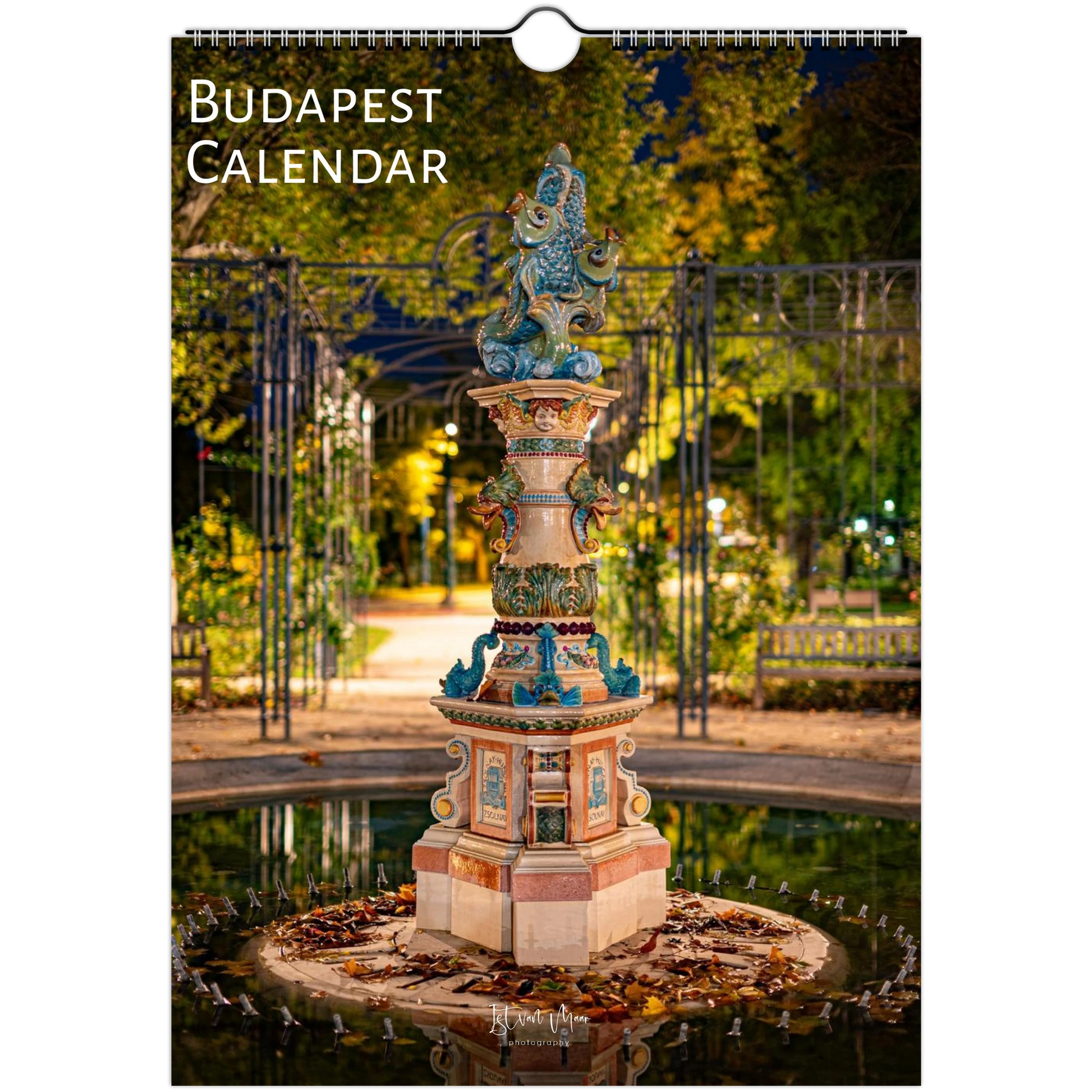 Budapest Calendar wall calendar cover featuring a nighttime photograph of a decorative fountain in a park with trees and a gate. The title 'BUDAPEST CALENDAR' appears at the top left, and a hanging hole is visible at the top center.