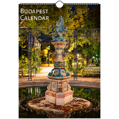 Budapest Calendar wall calendar cover featuring a nighttime photograph of a decorative fountain in a park with trees and a gate. The title 'BUDAPEST CALENDAR' appears at the top left, and a hanging hole is visible at the top center.