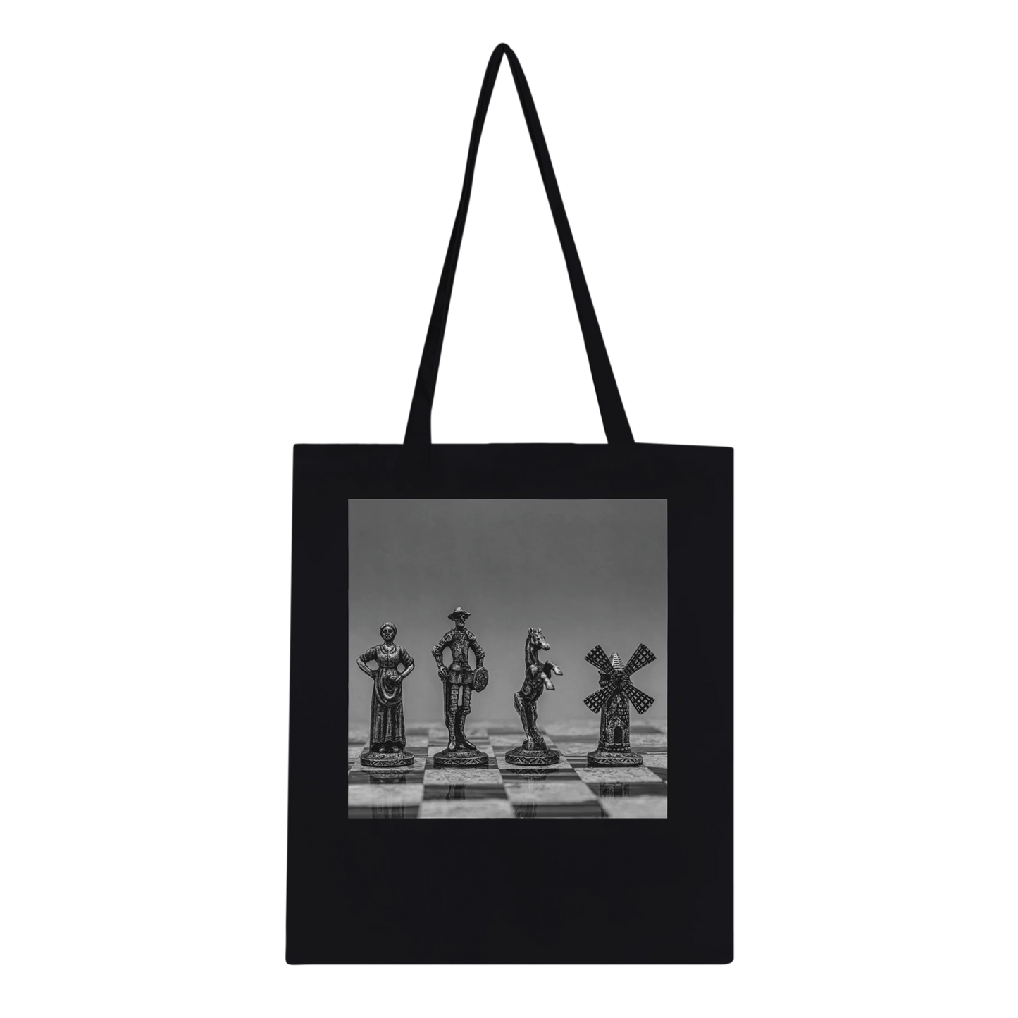 A black canvas tote bag with black shoulder straps, featuring a square black-and-white photographic print of chess pieces on a chessboard across the front. Ships worldwide by Istvan Maar Photography.