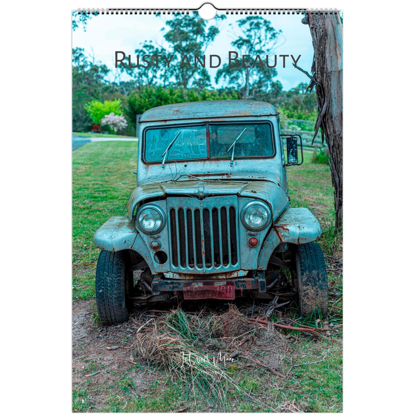 A spiral-bound wall calendar or print featuring a vintage weathered blue-green jeep parked outdoors on grass beside a tree, with the text 'Rusty and Beauty' across the top.