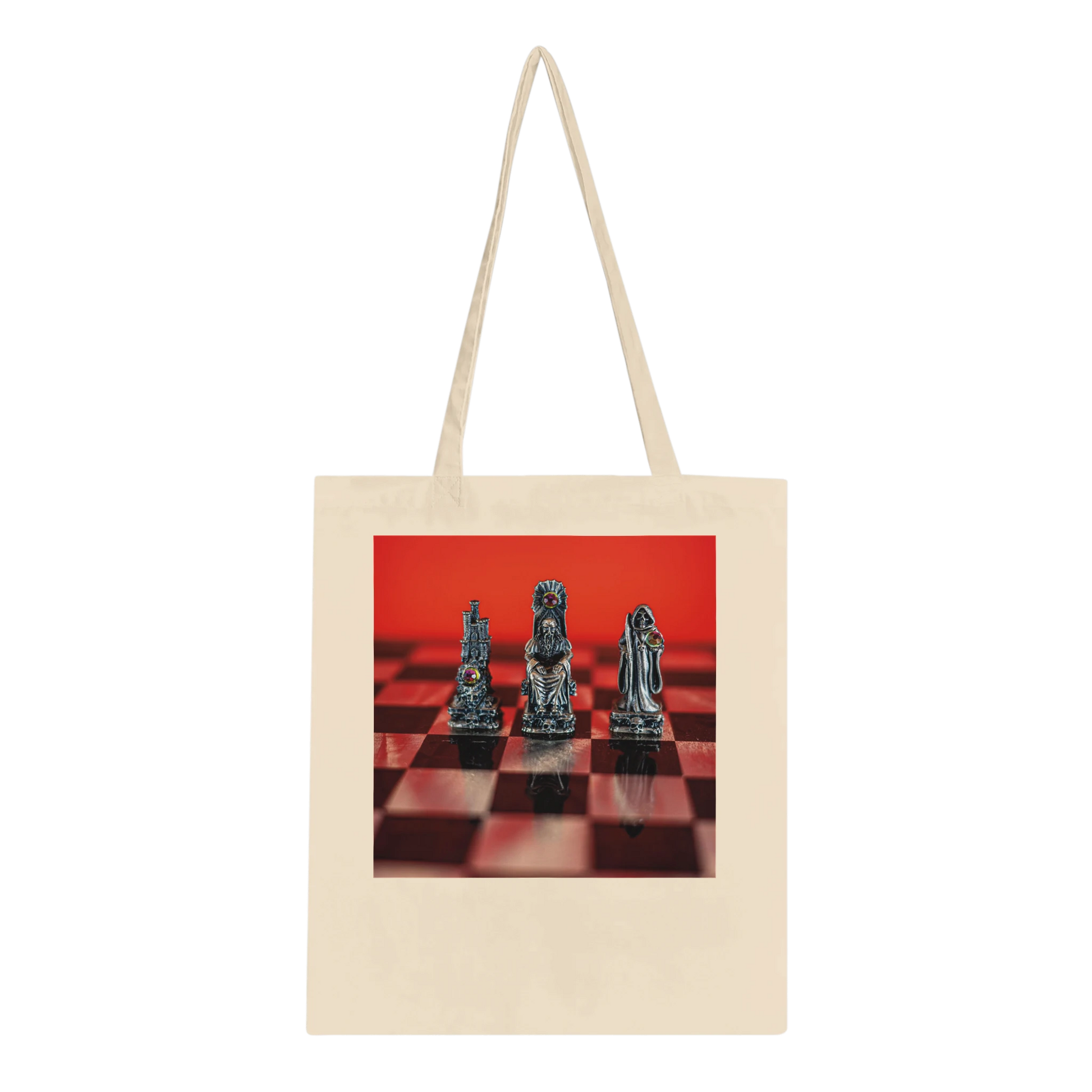 A natural canvas tote bag with long handles, featuring a rectangular printed graphic on the front of three metallic chess pieces on a red and black checkered board against a solid red background.