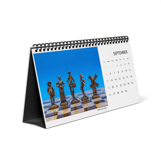 A spiral-bound desk calendar standing on its side, showing a September page with a blue sky and chess pieces printed on the front, photographed on a white background.