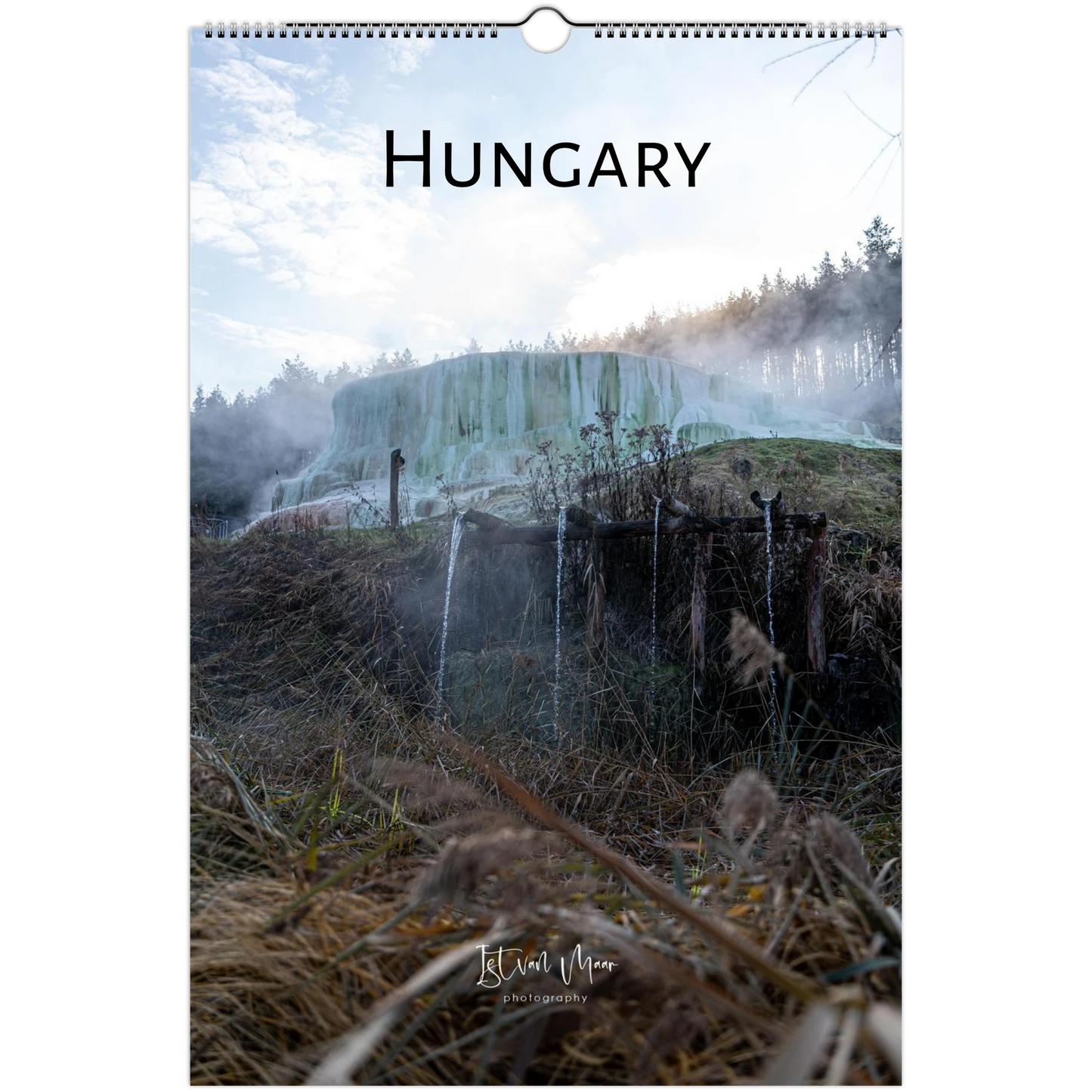A spiral-bound wall calendar or poster featuring a scenic photograph of a waterfall in Hungary, with the word 'HUNGARY' printed at the top and a small artist signature near the bottom.