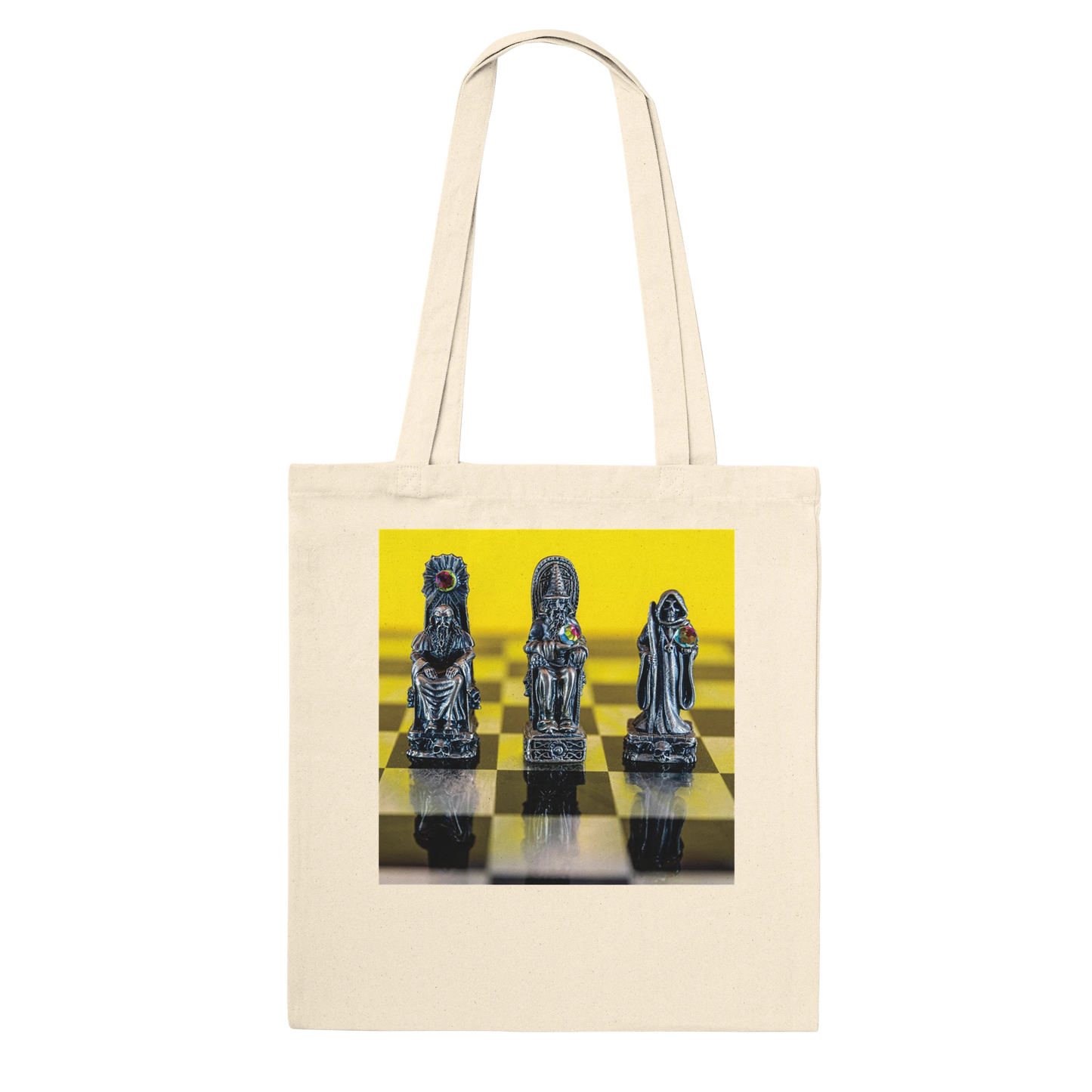 A cream canvas tote bag with a square graphic print on the front showing three metallic chess pieces on a yellow and black checkered board, set against a plain white background.