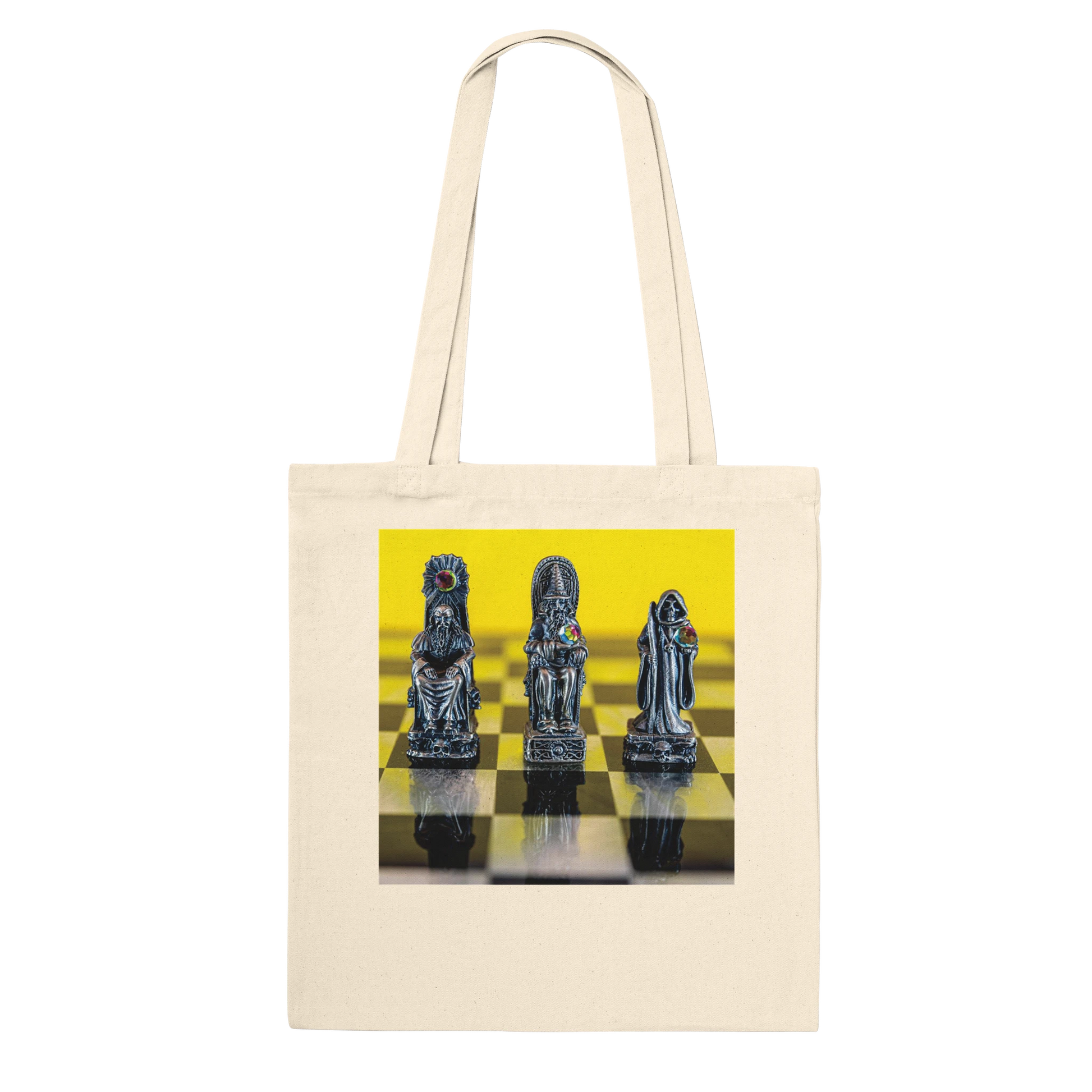 A cream canvas tote bag with a square graphic print on the front showing three metallic chess pieces on a yellow and black checkered board, set against a plain white background.
