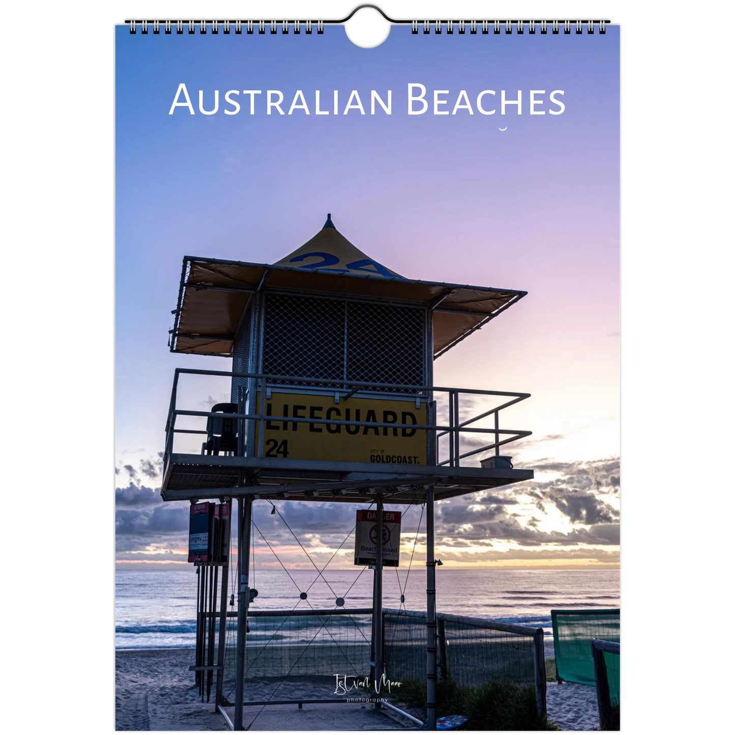 A spiral-bound wall calendar or print titled 'AUSTRALIAN BEACHES' shows a sunset beach scene with a lifeguard tower, ocean, and sky. The product is photographed straight-on against a white background.