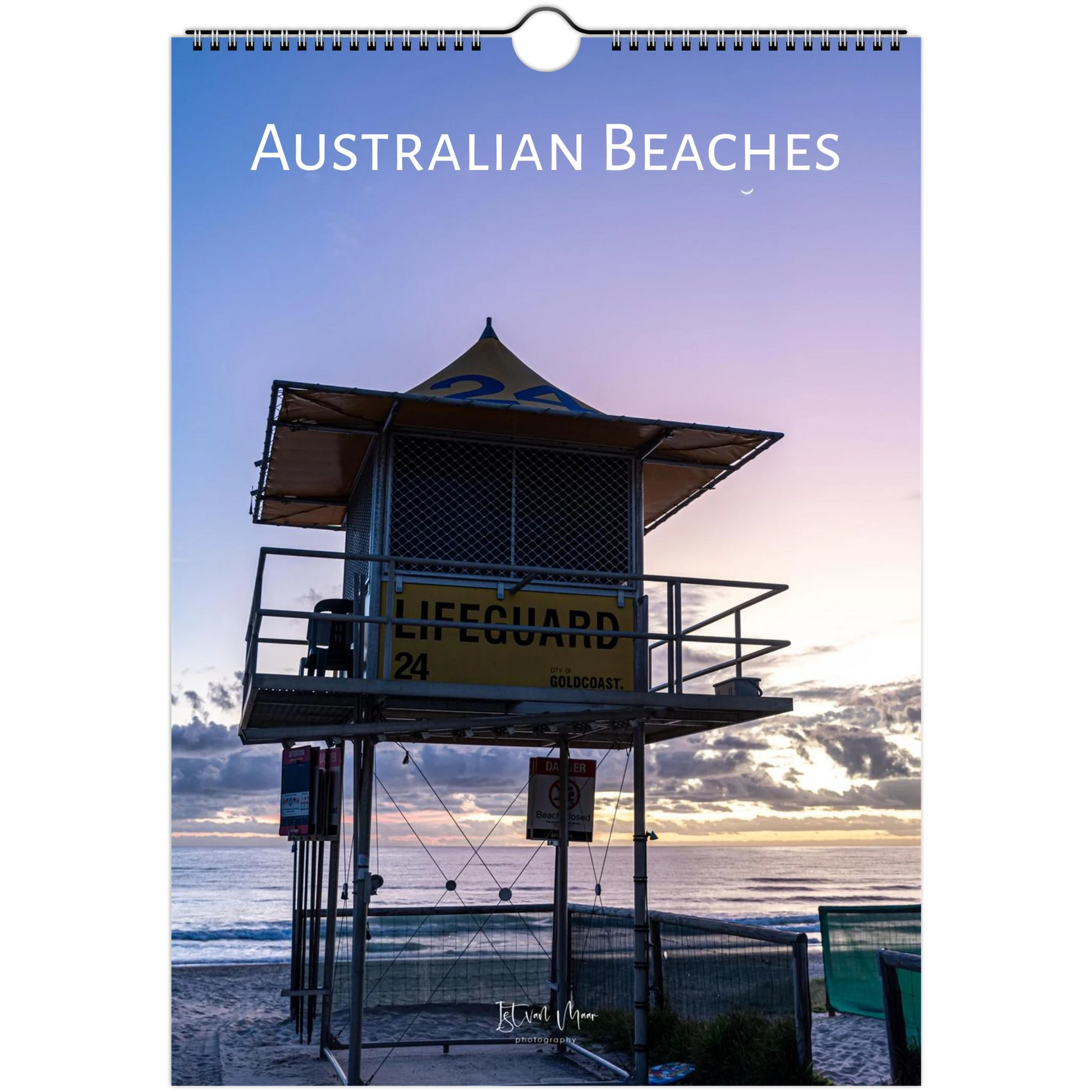 A spiral-bound wall calendar or print titled 'AUSTRALIAN BEACHES' shows a sunset beach scene with a lifeguard tower, ocean, and sky. The product is photographed straight-on against a white background.