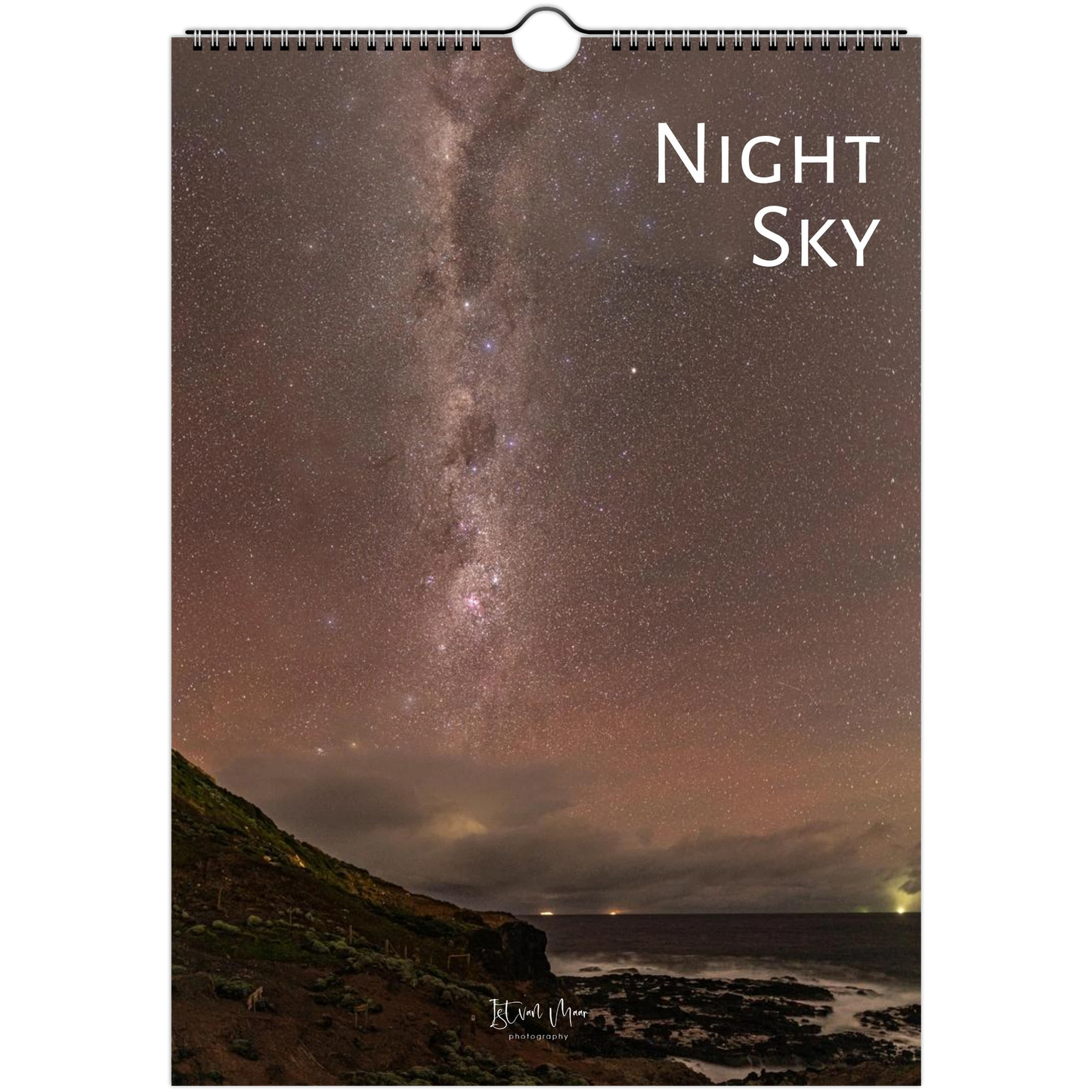 A spiral-bound wall calendar or print featuring a night sky photograph with the Milky Way over a rocky coastline. The words 'Night Sky' appear in white at the upper right, and a small artist signature is visible near the bottom.