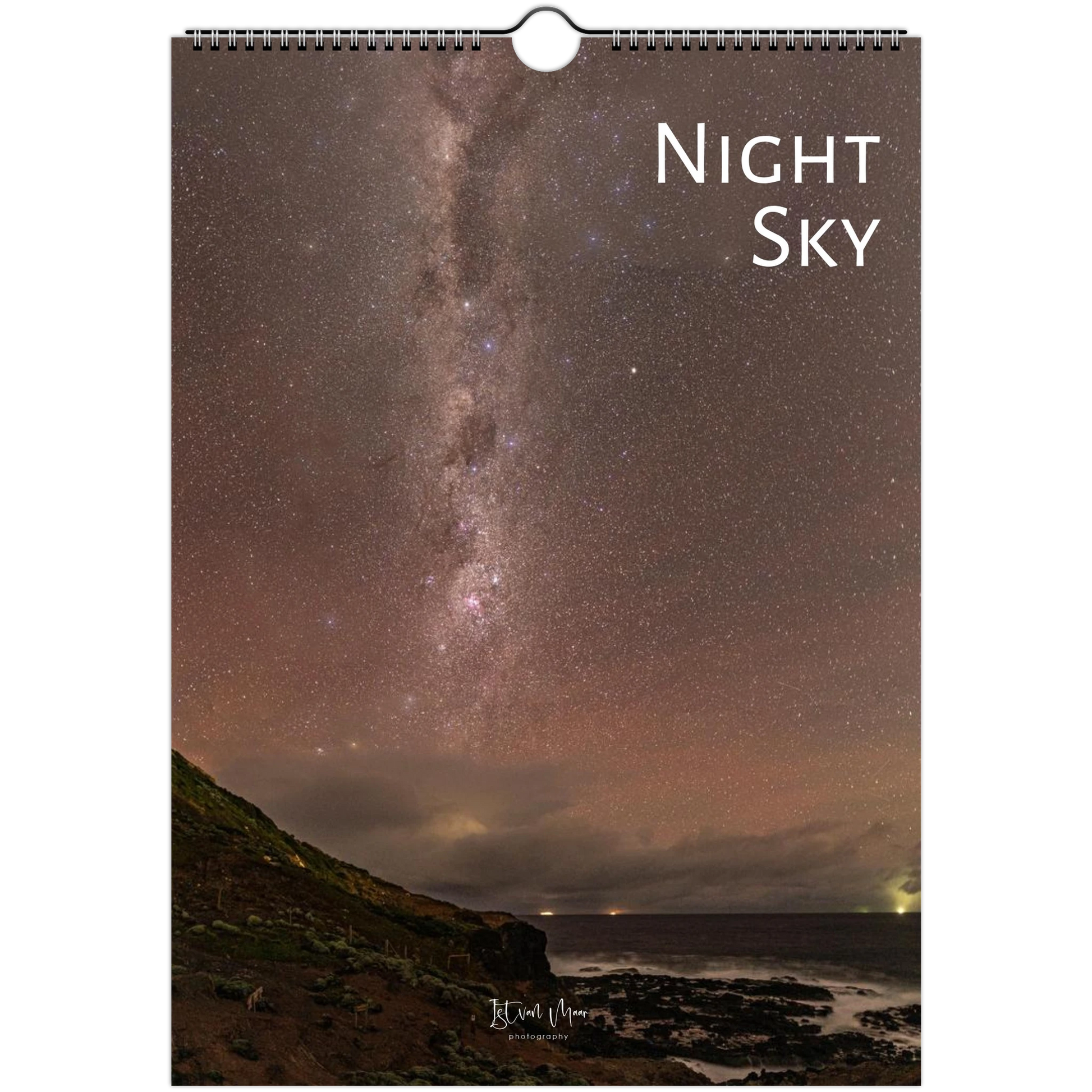A spiral-bound wall calendar or print featuring a night sky photograph with the Milky Way over a rocky coastline. The words 'Night Sky' appear in white at the upper right, and a small artist signature is visible near the bottom.