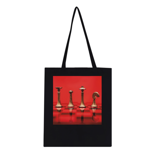 A black canvas tote bag with black shoulder straps, featuring a square graphic print on the front of four metallic chess pieces against a vivid red background.