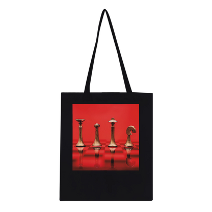 A black canvas tote bag with black shoulder straps, featuring a square graphic print on the front of four metallic chess pieces against a vivid red background.