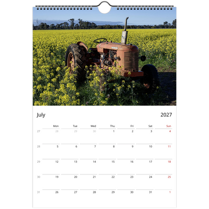 A single-page wall calendar spread showing a photograph of an old orange tractor in a yellow flower field on the top page, with a July 2027 calendar grid on the bottom page against a white background.