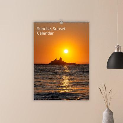 Calendar with a sunset design on a wall above a vase and plant.