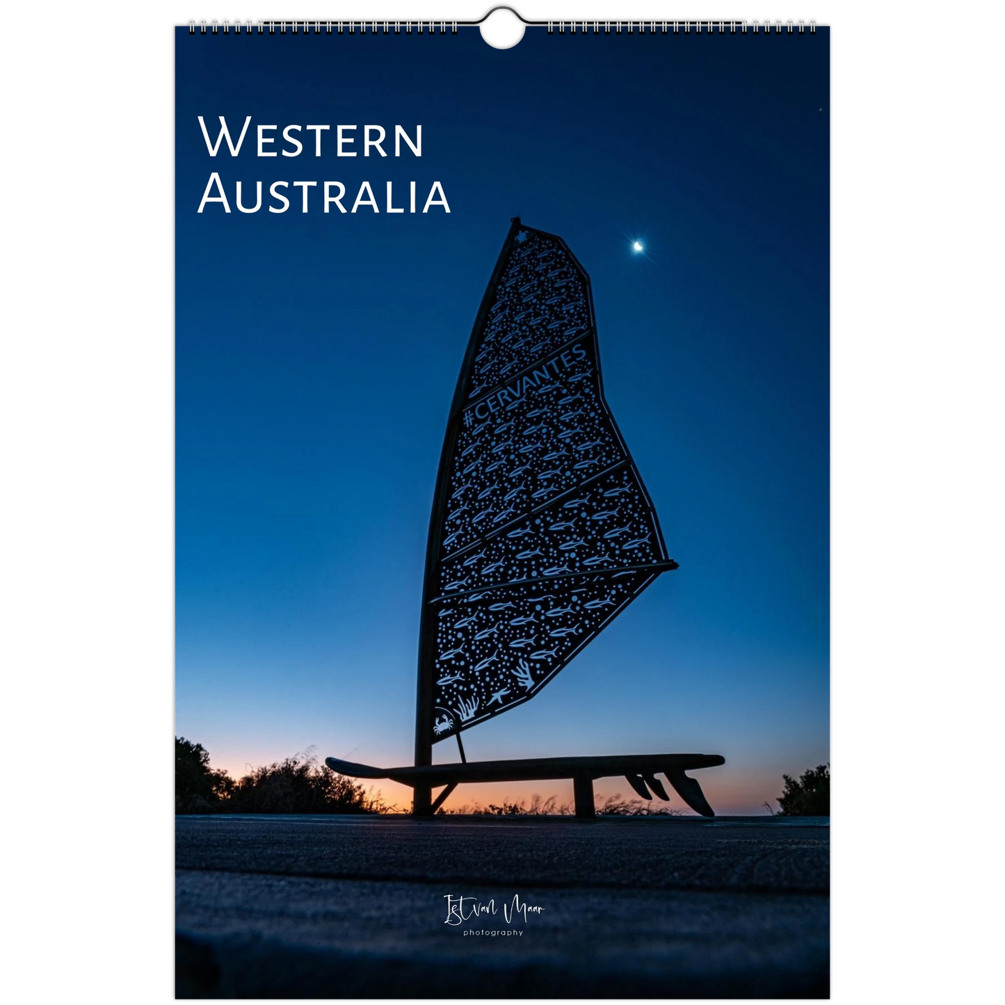 A vertical wall calendar or print featuring a scenic photograph of Western Australia at dusk or dawn, with a dark silhouette of a decorative sail-like sculpture against a deep blue sky. The words 'WESTERN AUSTRALIA' appear at the top, and a small photographer signature is visible near the bottom.