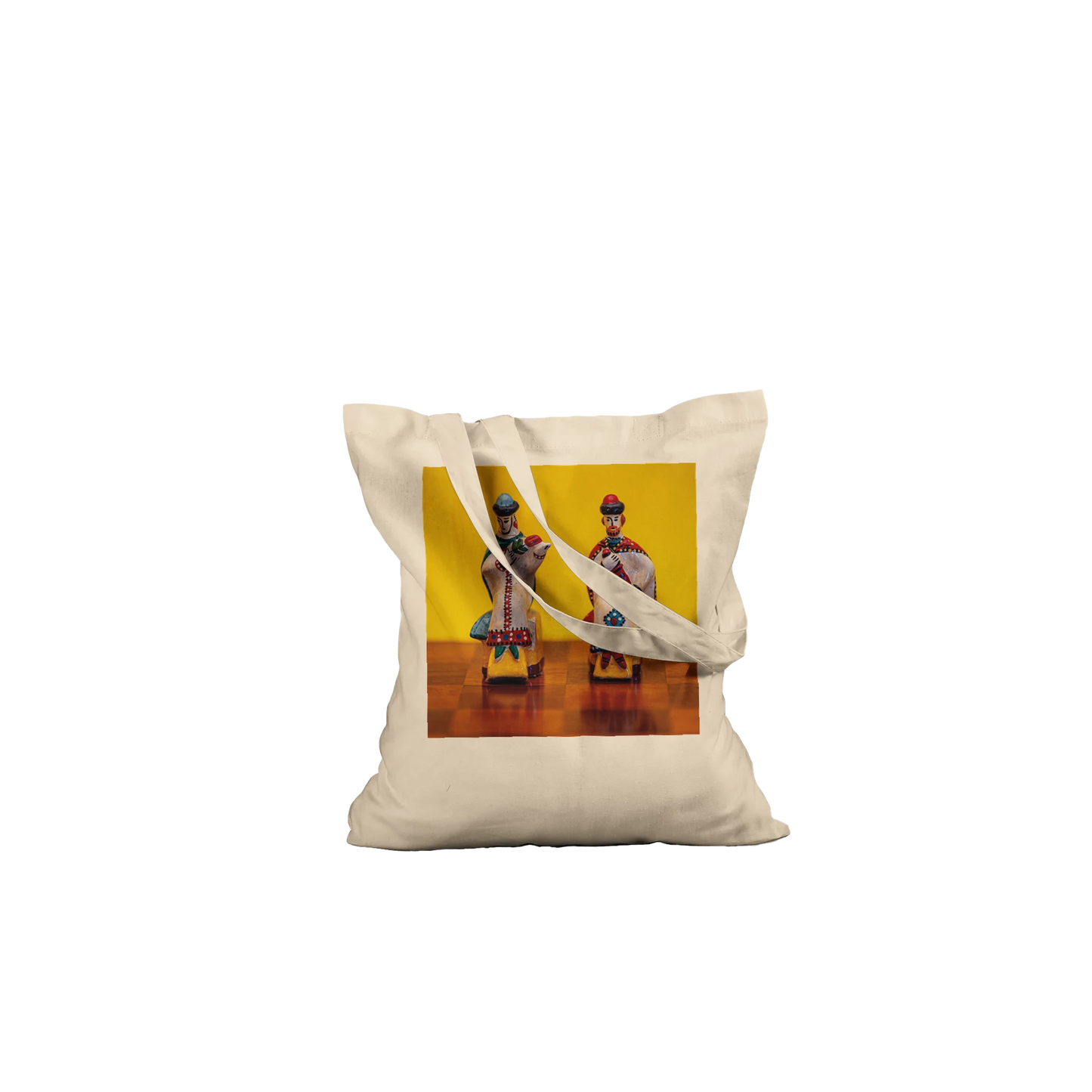 A natural canvas tote bag with two shoulder straps, featuring a square printed graphic on the front. The graphic shows two traditional Russian porcelain figurines against a bright yellow background.