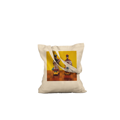 A natural canvas tote bag with two shoulder straps, featuring a square printed graphic on the front. The graphic shows two traditional Russian porcelain figurines against a bright yellow background.