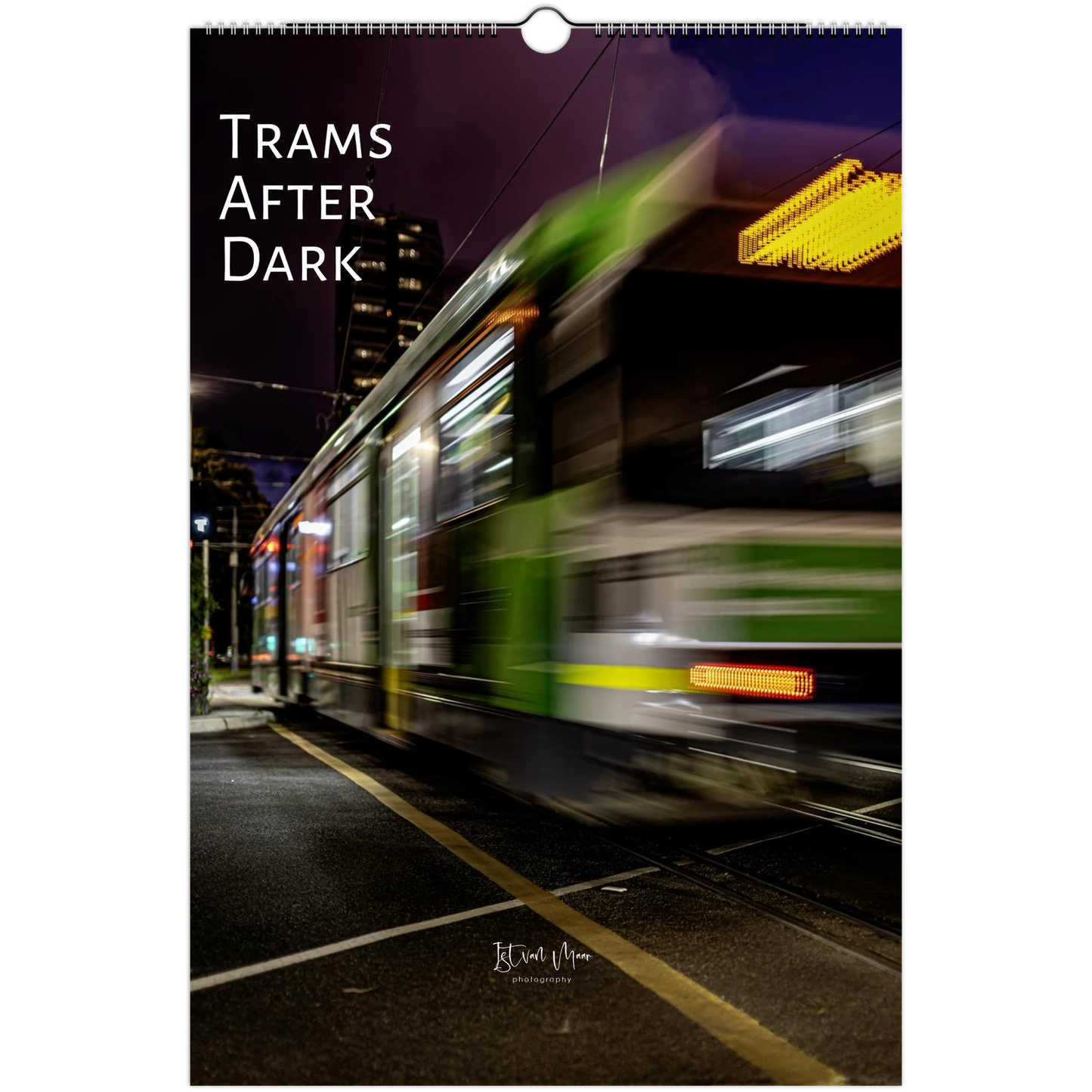 A hanging wall calendar or print featuring a nighttime photograph of a moving tram on a city street, with the title 'TRAMS AFTER DARK' in large white text at the top and a small photographer signature near the bottom.