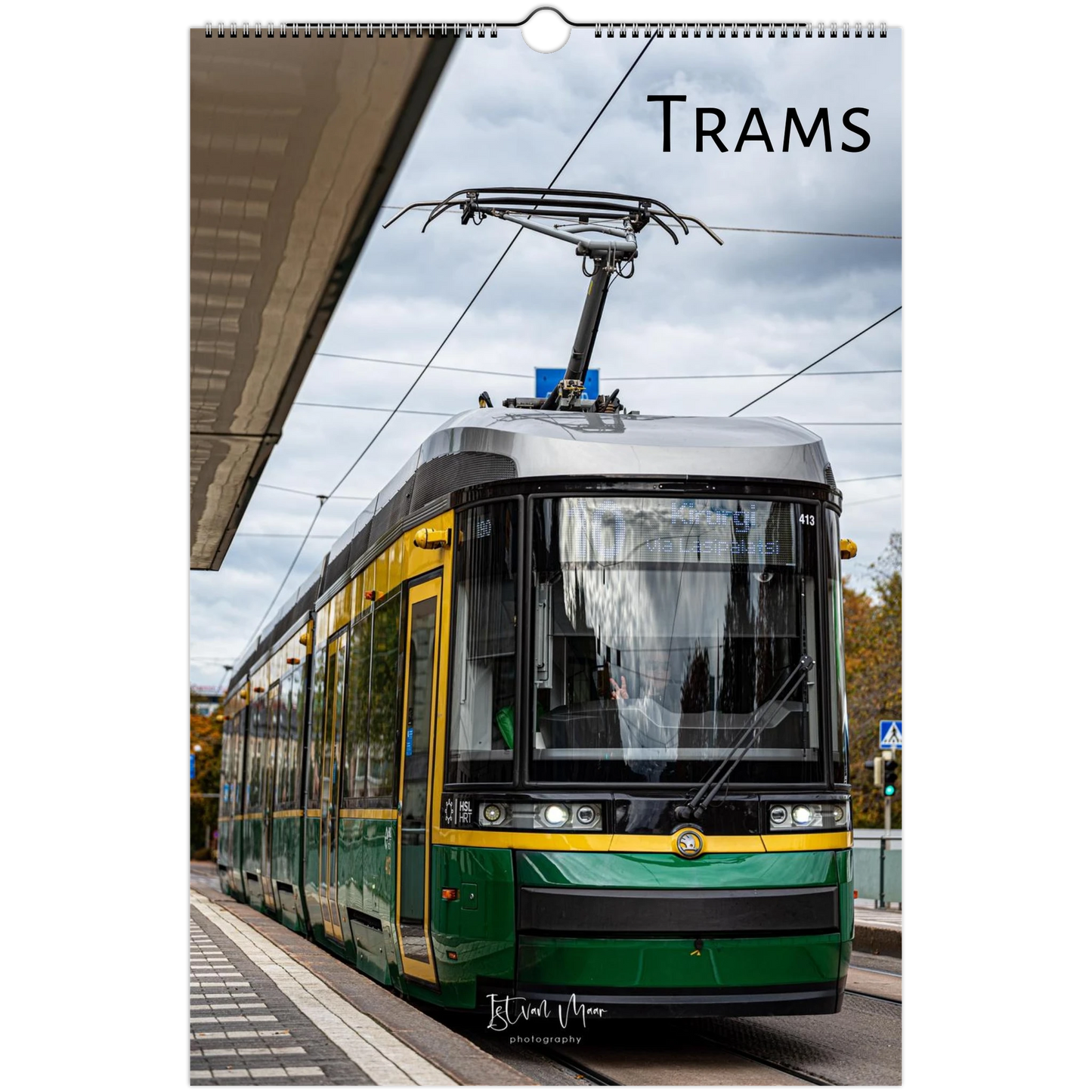 A spiral-bound wall calendar page featuring a photograph of a green and yellow tram on a city street under an overcast sky, with the word 'TRAMS' printed at the top. Original photography by Istvan Maar.