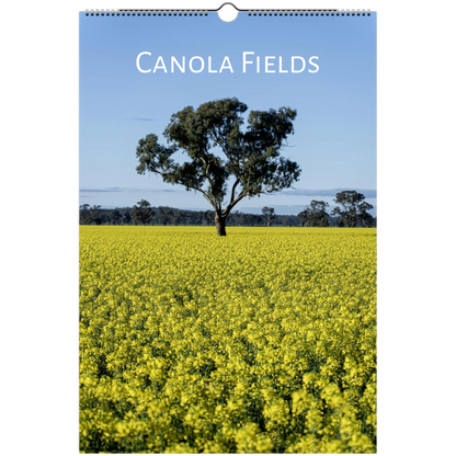 A spiral-bound wall calendar featuring a landscape photograph of a canola field with a single tree under a blue sky, with the text 'CANOLA FIELDS' at the top.