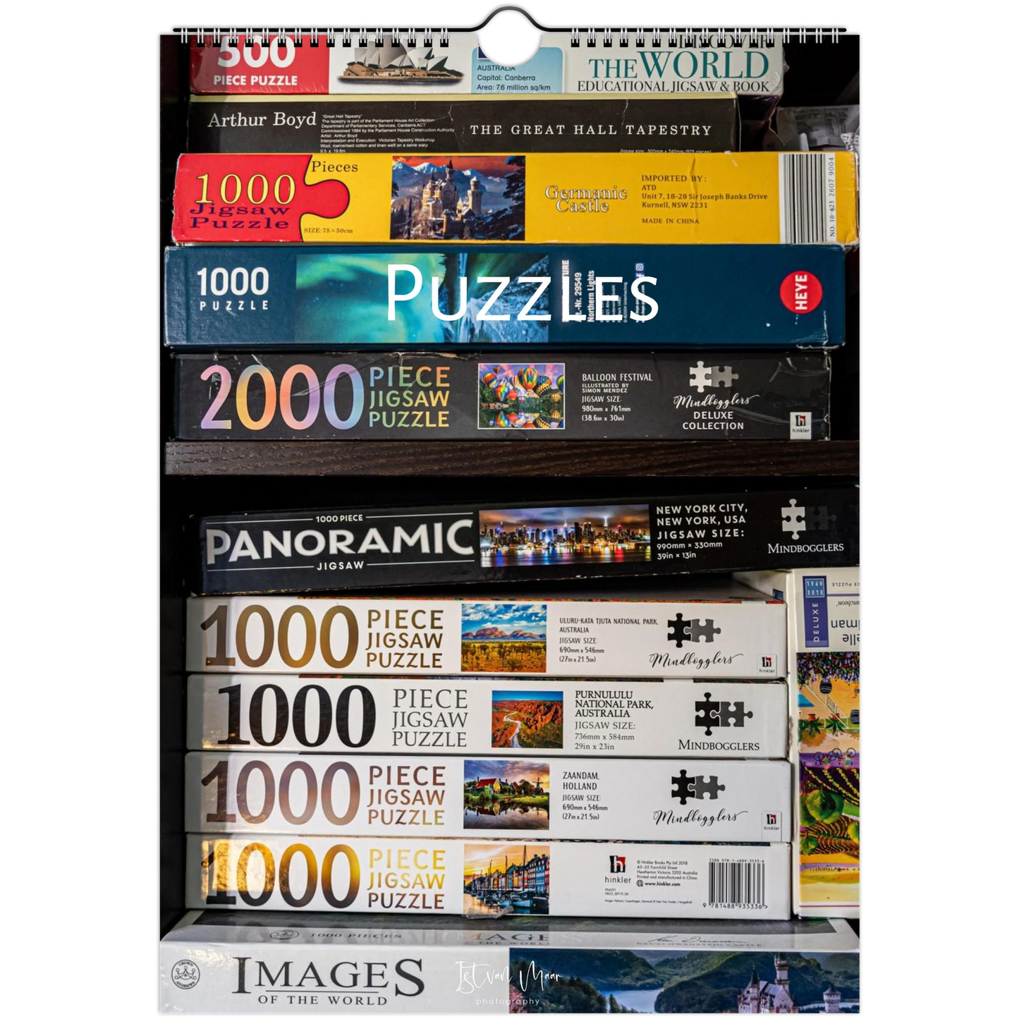A retail display shelf filled with various jigsaw puzzle boxes from brands like Woodland, Images of the World, and Millennium, showing puzzle piece counts ranging from 1000 to 3000.