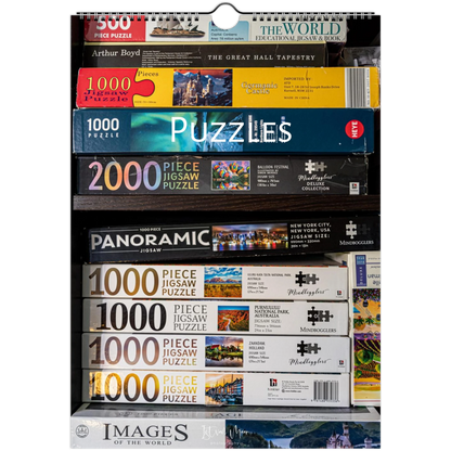 A retail display shelf filled with various jigsaw puzzle boxes from brands like Woodland, Images of the World, and Millennium, showing puzzle piece counts ranging from 1000 to 3000.