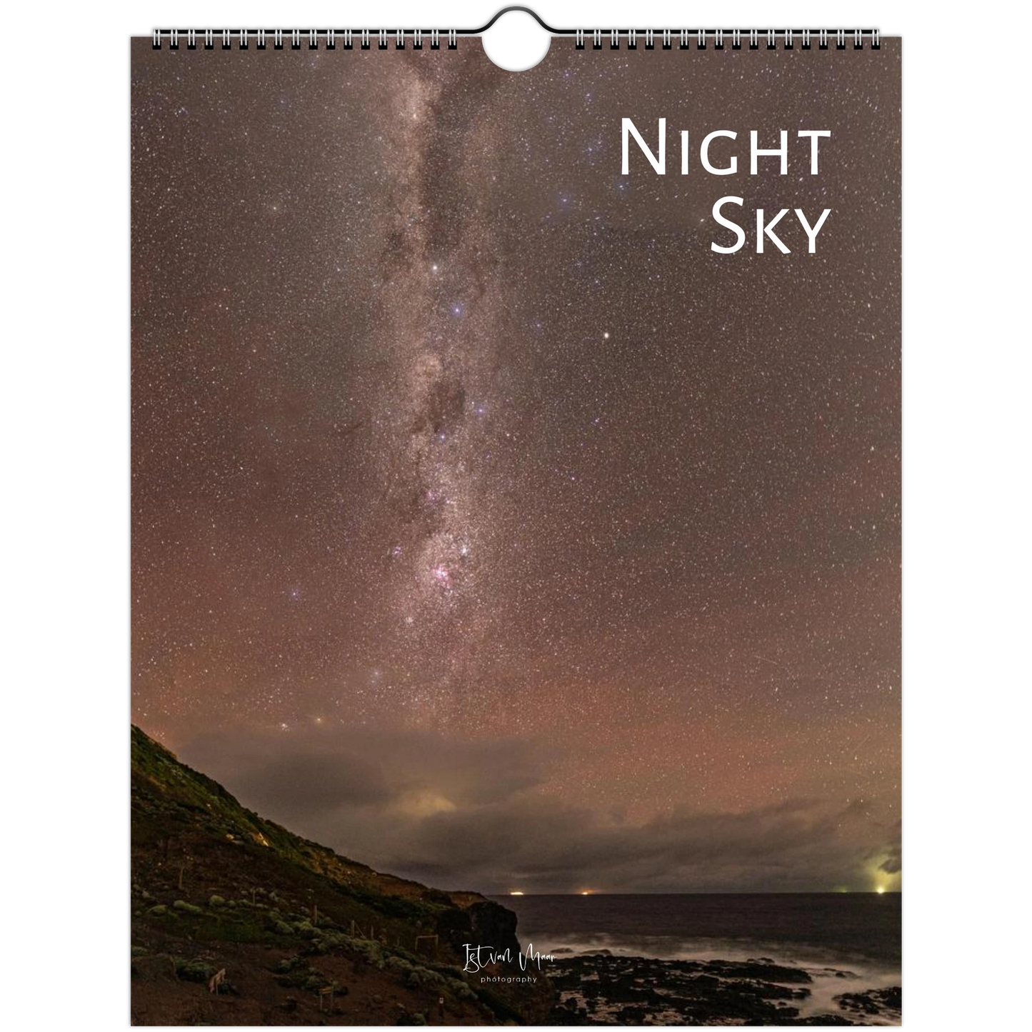 A spiral-bound wall calendar or print featuring a night sky photograph with the Milky Way over a dark shoreline. The words 'Night Sky' appear in white at the top right, and a small signature is visible near the bottom.