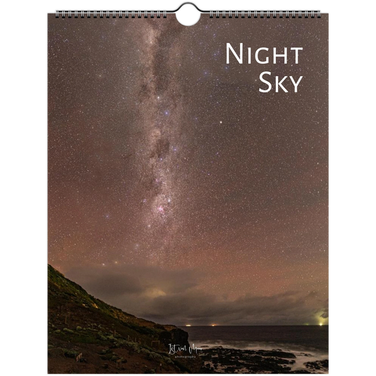A spiral-bound wall calendar or print featuring a night sky photograph with the Milky Way over a dark shoreline. The words 'Night Sky' appear in white at the top right, and a small signature is visible near the bottom.