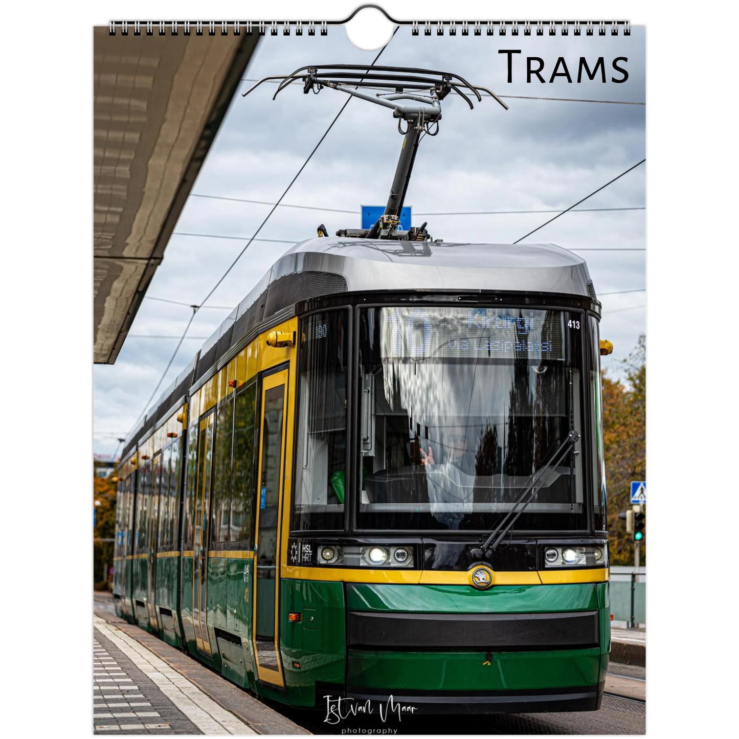 A spiral-bound wall calendar page featuring a photograph of a green and yellow tram at a station, with the word 'TRAMS' printed at the top and a small signature at the bottom.