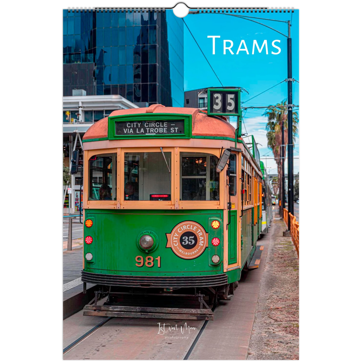 A vertical wall calendar page featuring a vintage green and cream tram on a city street, with the title 'TRAMS' printed at the top right. The calendar has a hanging ring at the top and a printed photo of the street scene on the front.