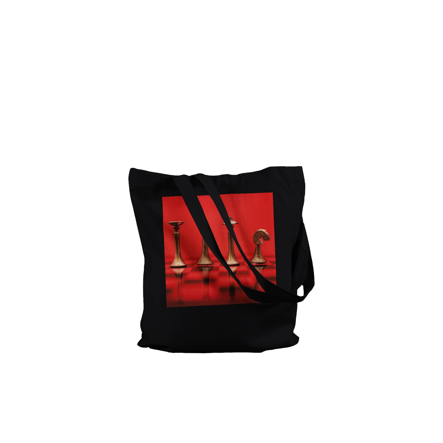 A black canvas tote bag with black shoulder straps, featuring a square graphic print on the front depicting metallic gold chess pieces on a vibrant red background.
