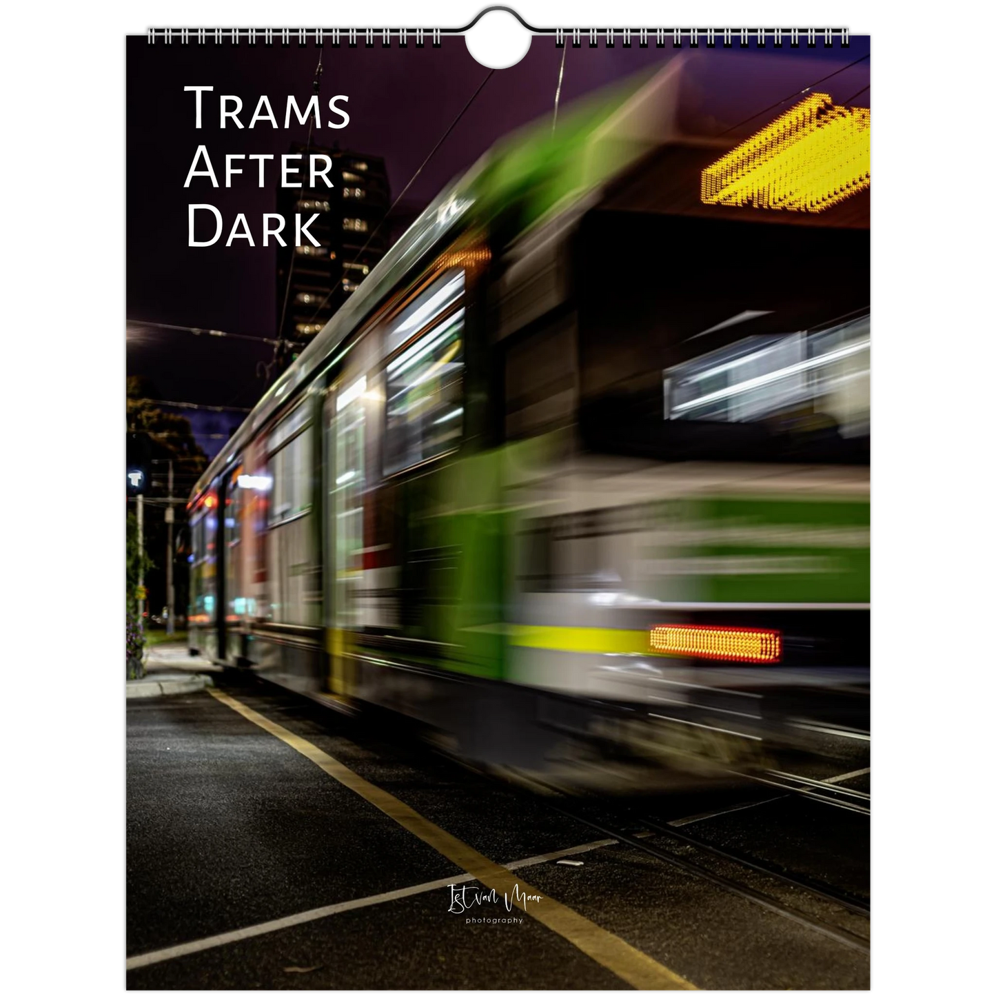 A spiral-bound wall calendar or print featuring a motion-blurred nighttime streetcar scene with the text 'TRAMS AFTER DARK' in white at the top left. The artwork shows a green and gray tram moving across a dark city street at night, with bright window lights and a yellow overhead light.